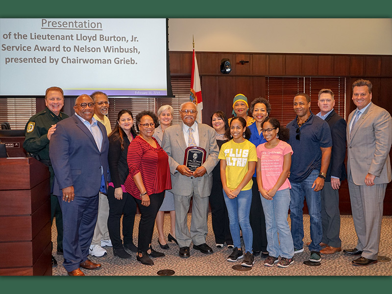 Nelson Winbush, center is surrounded friends, family, County Commissioners and members of Lloyd Burton Jr.’s family during Monday award ceremony.