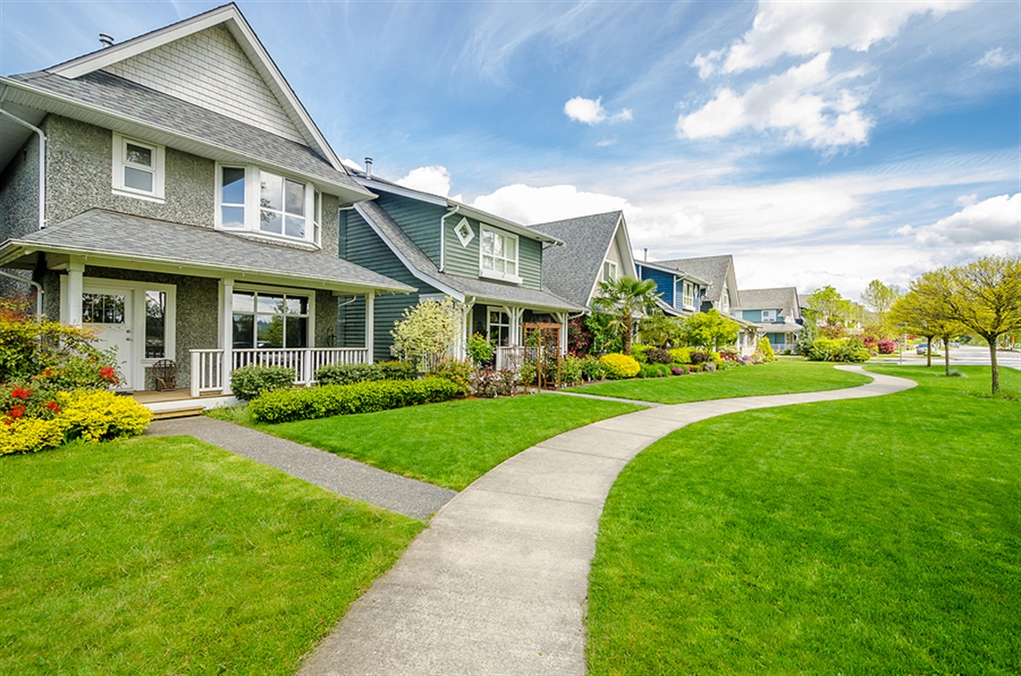 Neighborhood houses along nicely landscaped lawns and a sidewalk.