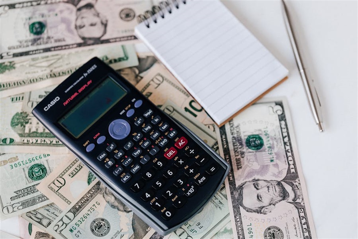 Calculator, pad and pen atop $5, $10, $20 bills.