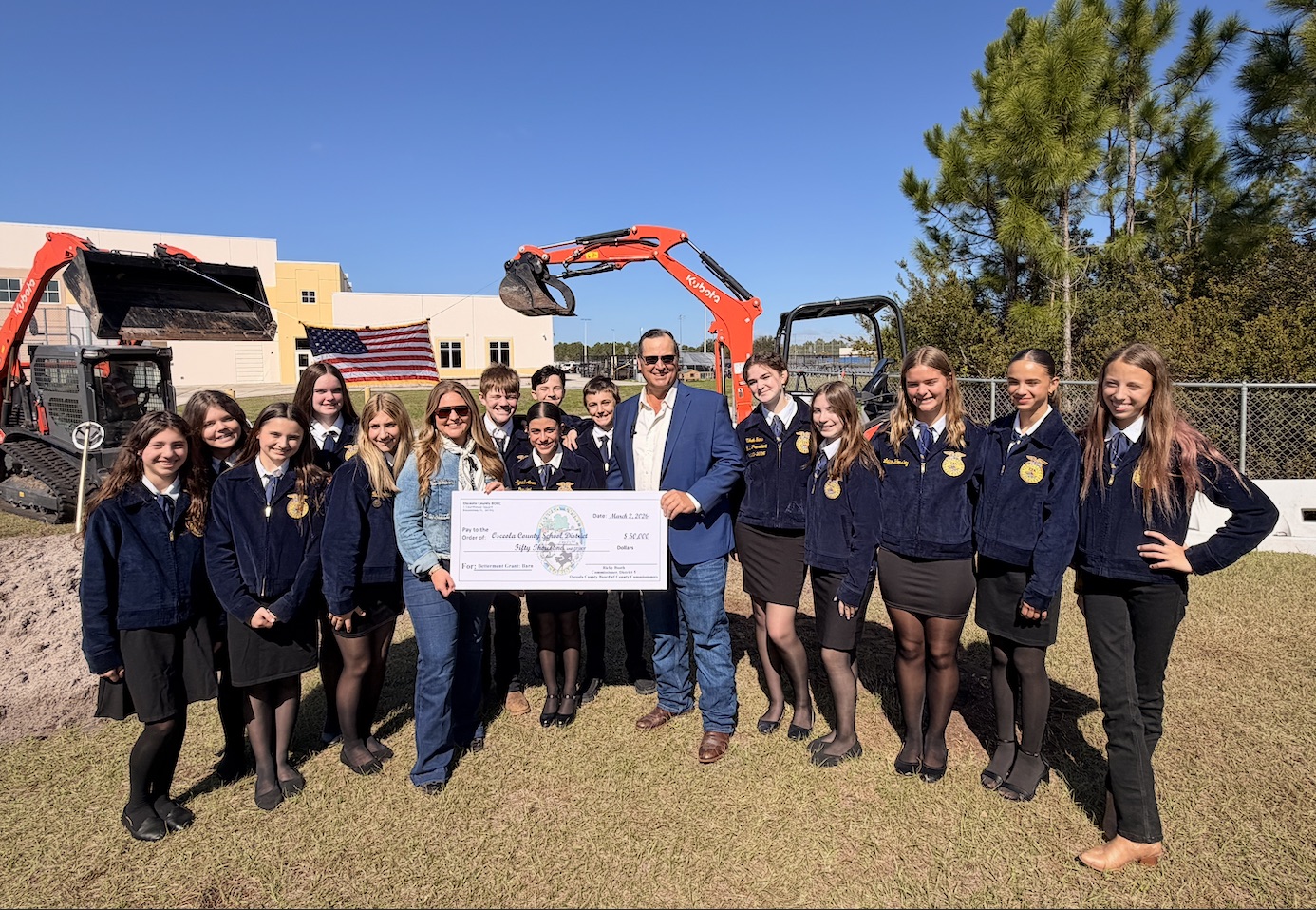 Commissioner Ricky Booth (C) presents a check to help build the Harmony Middle School pole barn.