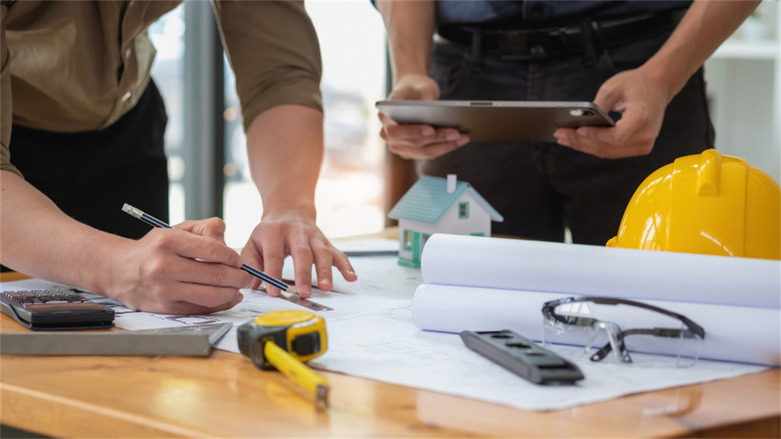 Two men working on building plans on a drafting table